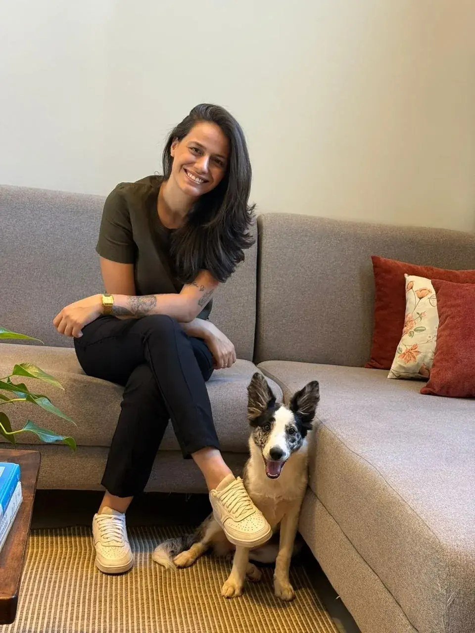 Dra. Mariana Neves sentada no sofá, sorrindo, com um cachorro sentado aos seus pés