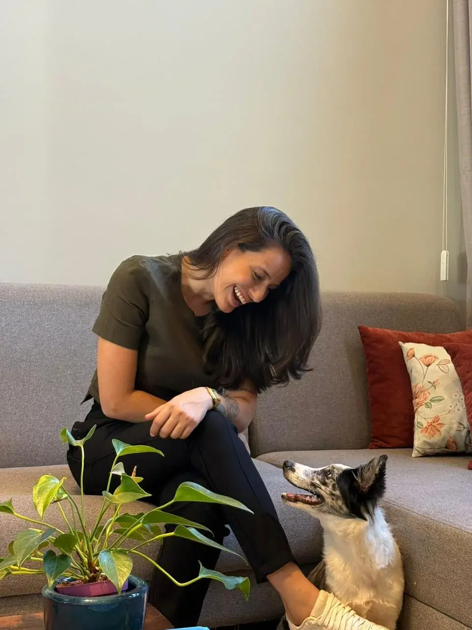 Dra. Mariana Neves rindo enquanto brinca com um cachorro na sala de casa